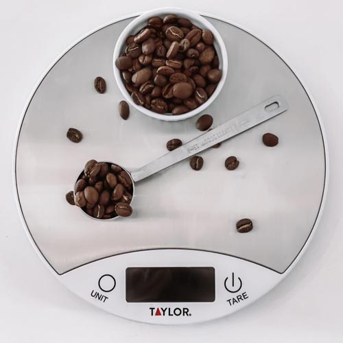 Whole coffee beans shown on a scale and in a tablespoon